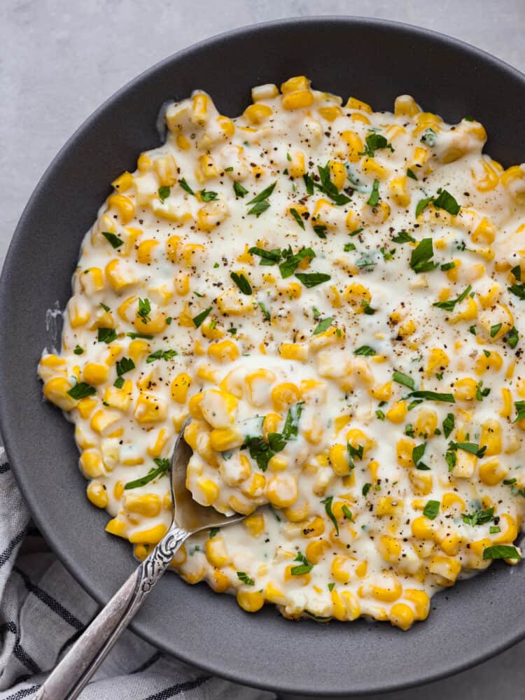 The ultimate side dish, this quick and easy creamed corn recipe is one you'll come back to again and again! It's buttery, creamy, and the perfect blend of savory and sweet! Top-down view of creamed corn in a black bowl, ready to serve.