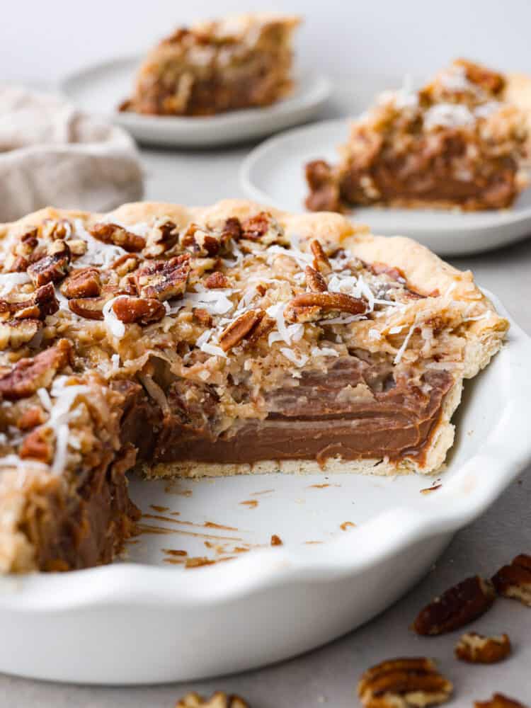 This decadent dessert is everything you love about German chocolate cake in one easy-to-make pie! Layers of chocolate custard, perfectly sweet shredded coconut, and salted pecans all in a golden, flaky crust. It's the perfect addition to your Thanksgiving table! German chocolate pie in a pie dish with a slice cut out of it.