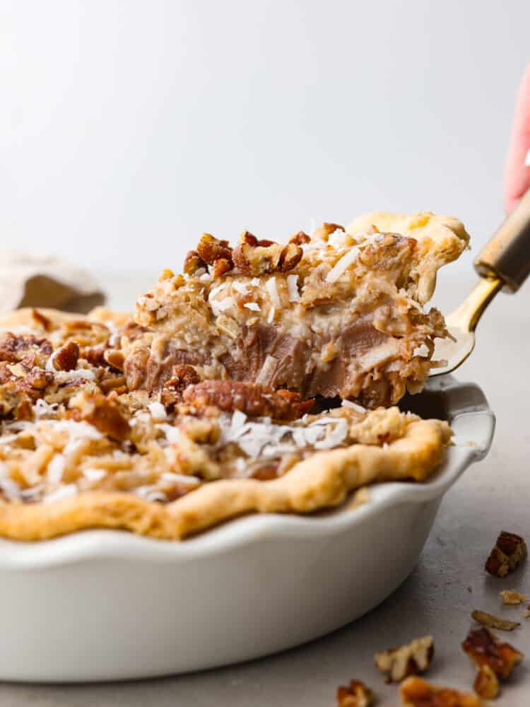 This decadent dessert is everything you love about German chocolate cake in one easy-to-make pie! Layers of chocolate custard, perfectly sweet shredded coconut, and salted pecans all in a golden, flaky crust. It's the perfect addition to your Thanksgiving table! A slice of German chocolate pie being served with a cake spatula.