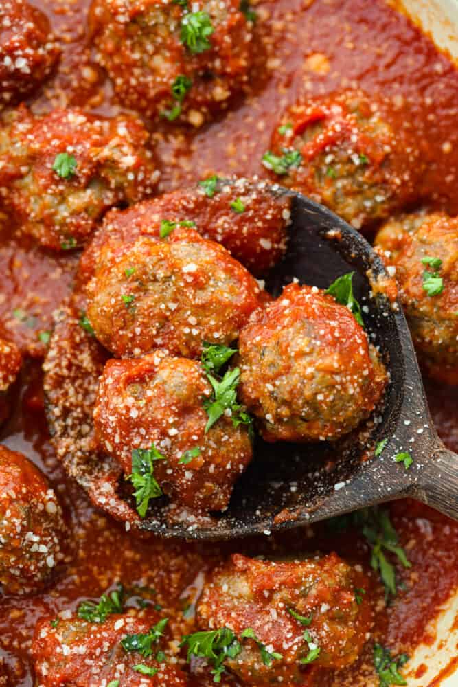 Whether you're making subs or spaghetti, these classic oven-baked meatballs are perfect for all of your favorite recipes. They're perfectly juicy and flavored with delicious seasonings and parmesan cheese! Closeup of 3 meatballs in a wooden spoon.