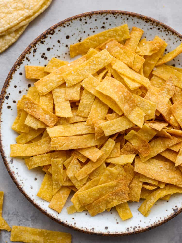These delicious and easy air fryer tortilla strips are the perfect topping for any of your delicious salads or Mexican dishes! They are crispy, seasoned, and so good that you will want to put them on everything! A close up of a plate filled with air fryer tortilla strips.