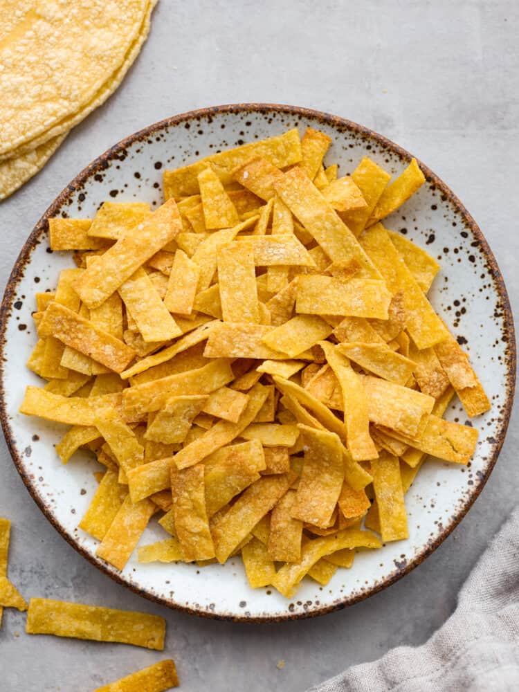These delicious and easy air fryer tortilla strips are the perfect topping for any of your delicious salads or Mexican dishes! They are crispy, seasoned, and so good that you will want to put them on everything! A plate with cooked tortilla strips.