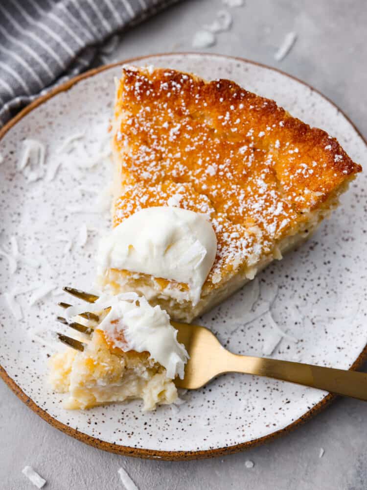 Don't be fooled by the name, this impossible pie is one of the easiest pies you'll ever make! Called "impossible" because it magically forms its own crust, you can have this pie ready for the oven in just 7 minutes. This pie is a classic for a reason- the creamy custard filling and crunchy topping are irresistible! Closeup of a slice of pie. There is a small bite taken out of it with a gold metal fork.