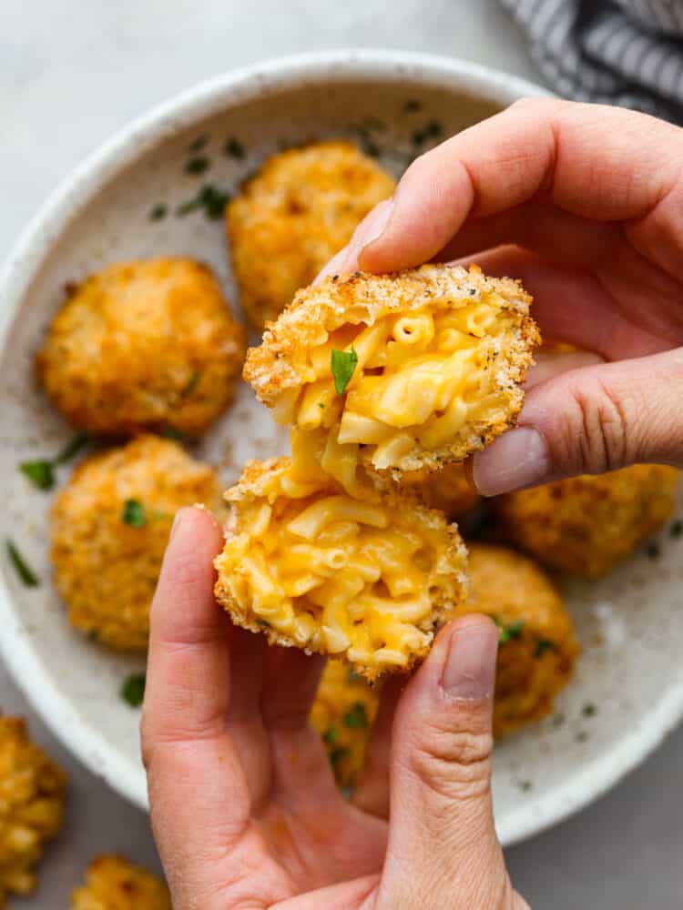 These air fryer mac and cheese balls are crunchy, gooey, and full of delicious cheesy flavor! They are sure to be a hit with your kids or dinner guests, and you'll get this recipe requested again and again. Someone holding a Mac and cheese ball that is broken in half.