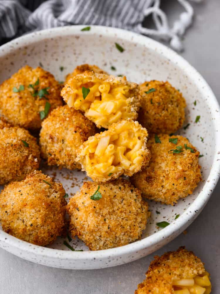These air fryer mac and cheese balls are crunchy, gooey, and full of delicious cheesy flavor! They are sure to be a hit with your kids or dinner guests, and you'll get this recipe requested again and again. A bowl of Mac and cheese balls, one on top that is broken open.