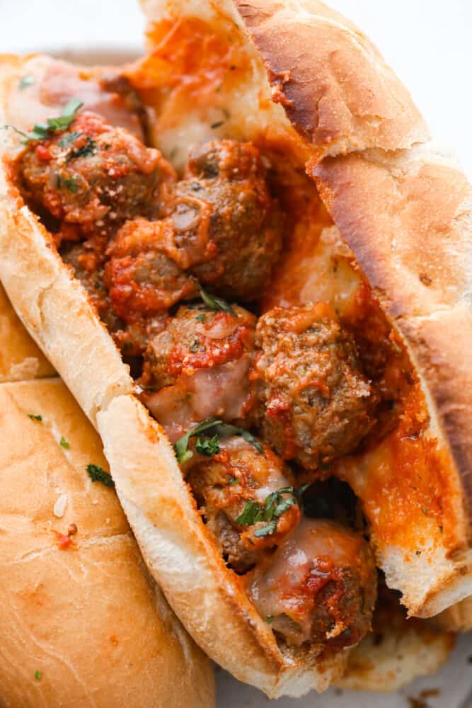 This easy meatball sub is always a favorite for both kids and adults. From the juicy meatballs smothered in marinara sauce to the toasted bun and melty cheese on top...it's the perfect sandwich for game day or any day! Close up view of a meatball sub opened and full of meatballs and marinara. Garnished with chopped basil on top.