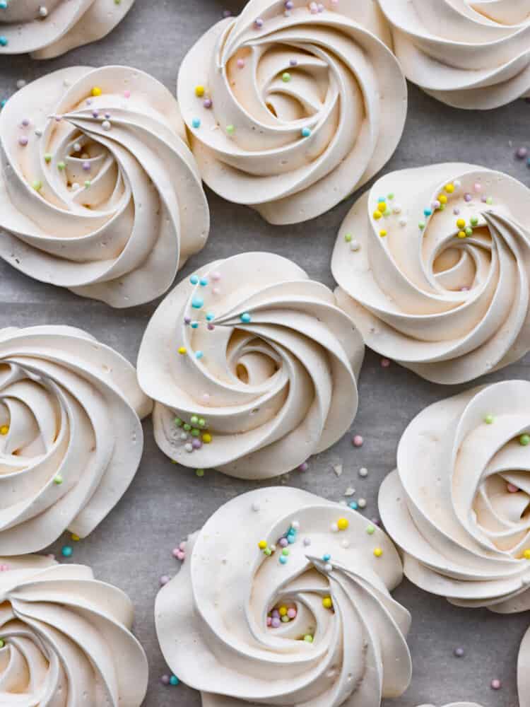 Meringue cookies are crispy on the outside and chewy on the inside. The whipped egg white base just melts in your mouth and tastes absolutely divine. They are a beautiful dessert for any occasion! Meringue cookies with colorful sprinkles on top sitting on top of parchment.