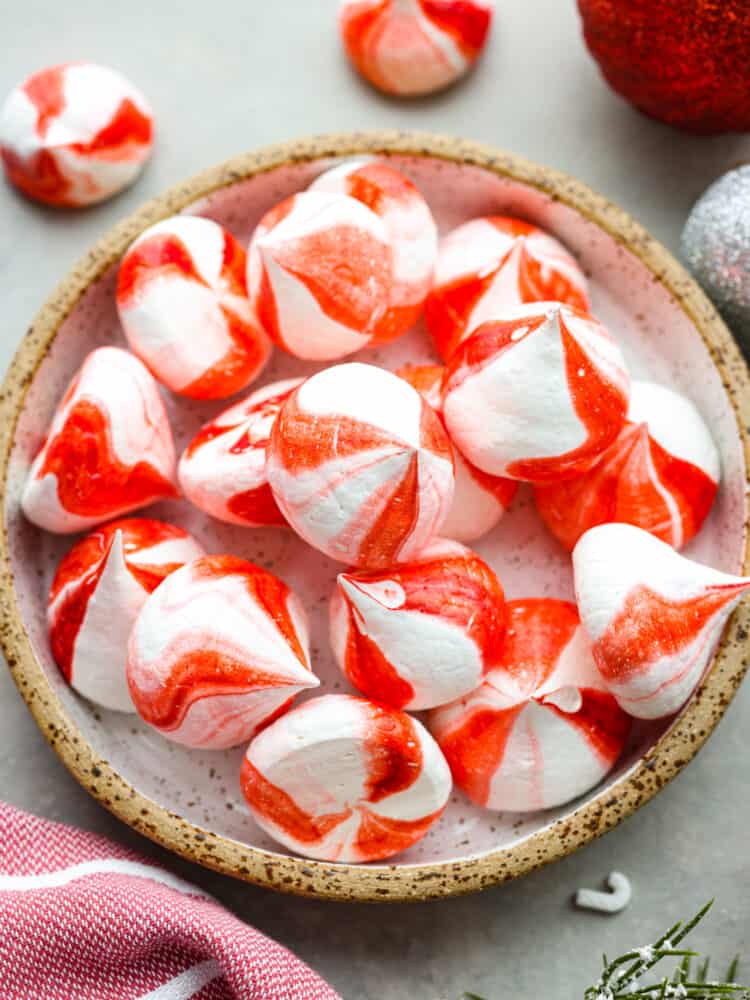 Peppermint Meringue Kisses are crunchy on the outside with a soft and chewy middle, and a peppermint flavor that is sweet and refreshing.ย They are the cutest little candies and are perfect for gifting this holiday season! Peppermint meringue kisses in a candy dish on a table with ornaments next to it.