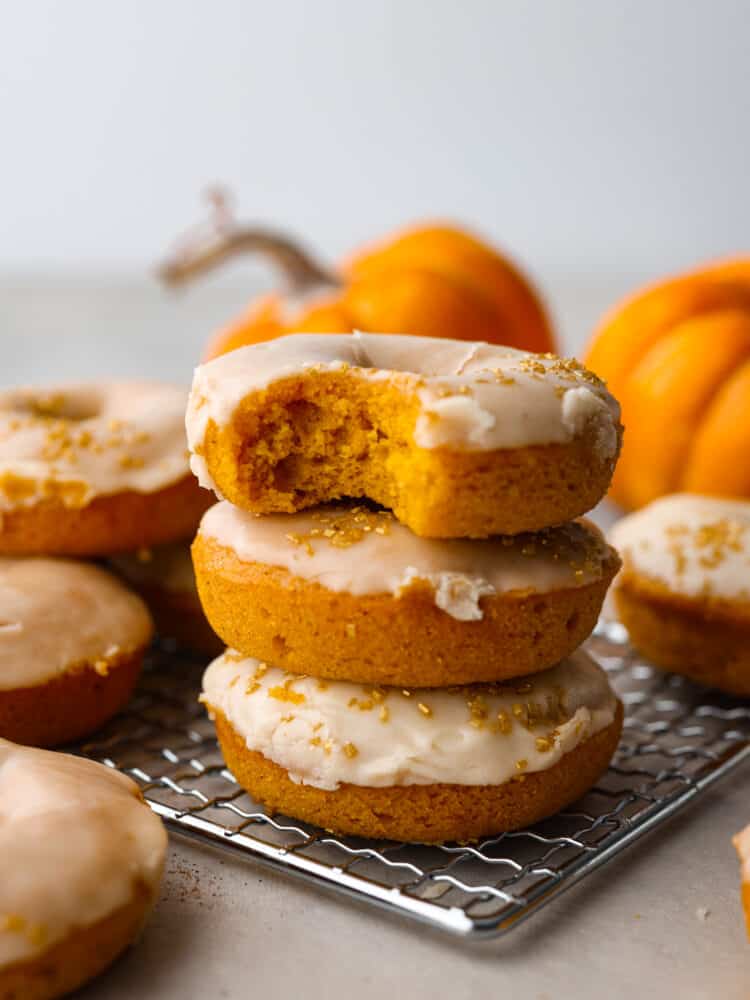 Meet your new favorite fall treat- moist, spiced pumpkin donuts covered in a decadent brown butter glaze! They cook in 15 minutes for a quick and delicious fall breakfast or dessert. With how amazing they are, they'll disappear in no time! A stack of 3 donuts on a wire rack.