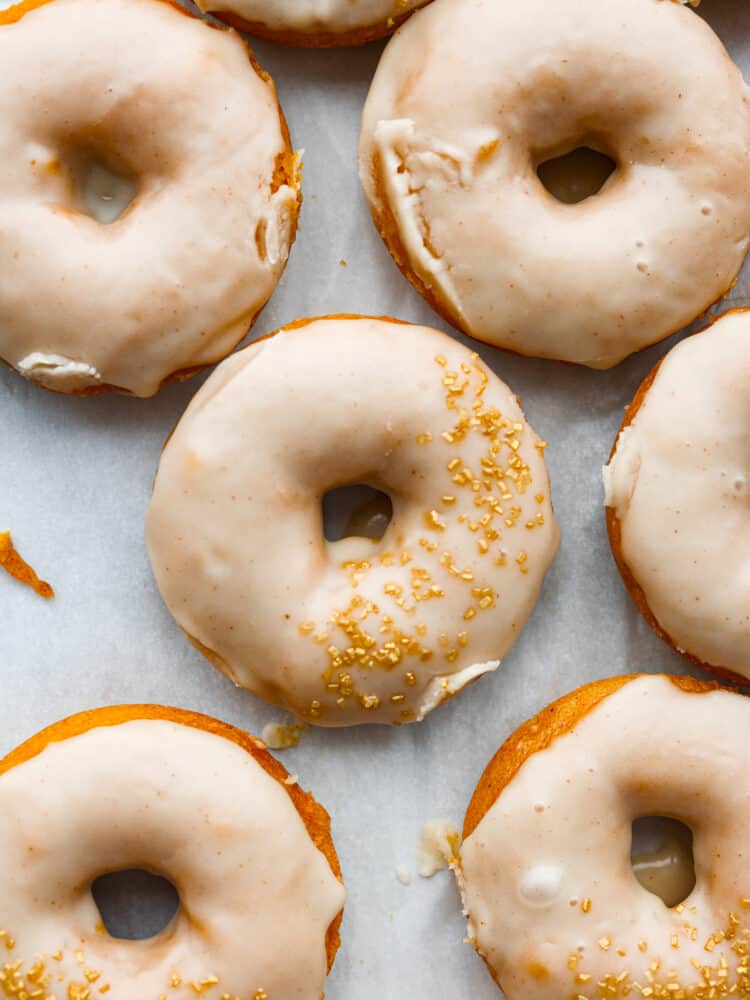 Meet your new favorite fall treat- moist, spiced pumpkin donuts covered in a decadent brown butter glaze! They cook in 15 minutes for a quick and delicious fall breakfast or dessert. With how amazing they are, they'll disappear in no time! Pumpkin donuts with brown butter frosting laid out on parchment paper.