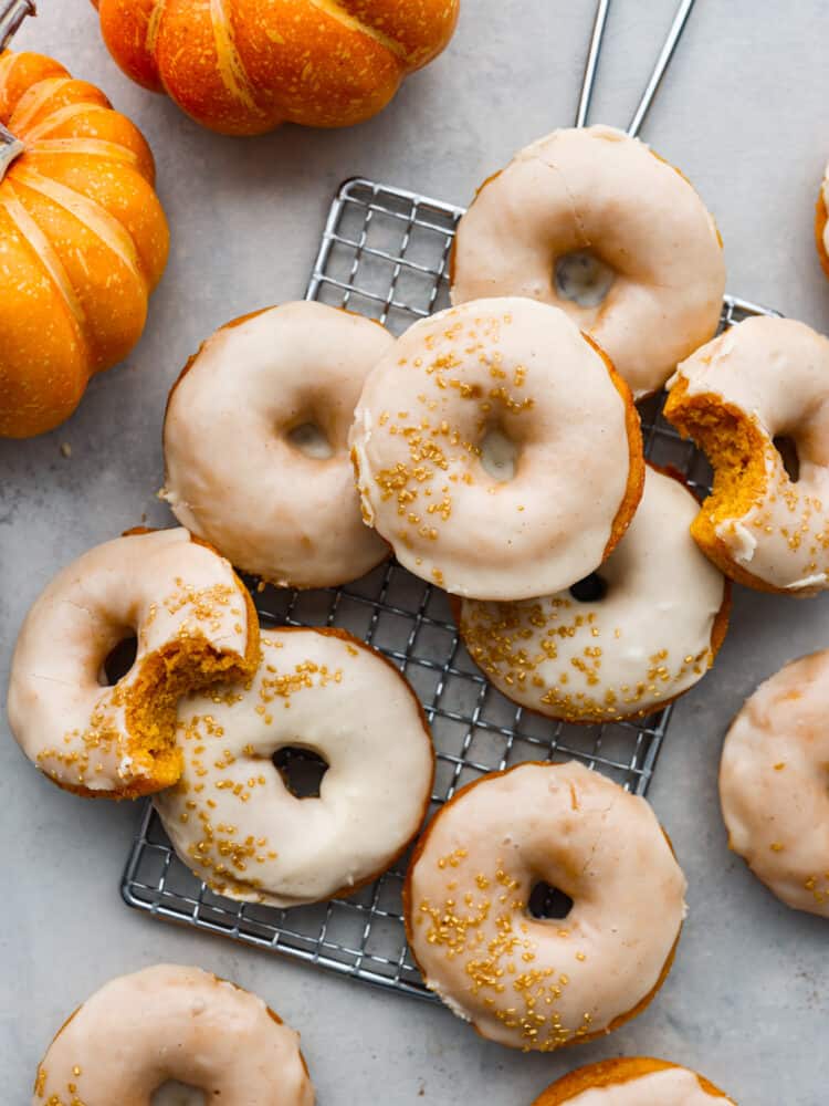 Meet your new favorite fall treat- moist, spiced pumpkin donuts covered in a decadent brown butter glaze! They cook in 15 minutes for a quick and delicious fall breakfast or dessert. With how amazing they are, they'll disappear in no time! Top-down view of multiple pumpkin donuts on a wire rack. 2 have bites taken out of them.