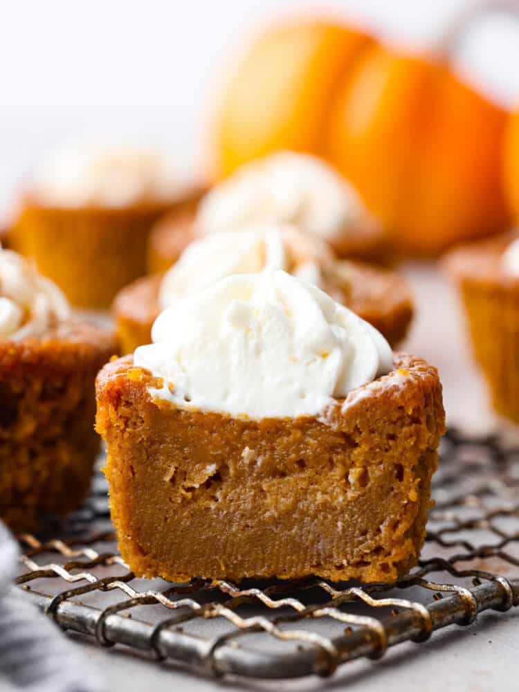 These moist and tender pumpkin pie cupcakes are all of the things you love about pumpkin pie, just bite-sized! Topped with amazing cream cheese whipping cream, these will be the BEST cupcakes you'll ever eat!! Front view of a frosted cupcake cut in half.