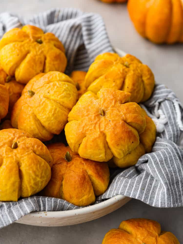 These pumpkin dinner rolls are the perfect, festive side dish to add to any fall meal! They not only taste like pumpkin but they are shaped just like one as well! Impress all of your guests by making these rolls and taking your holiday celebrations to the next level. A basket of pumpkin dinner rolls.
