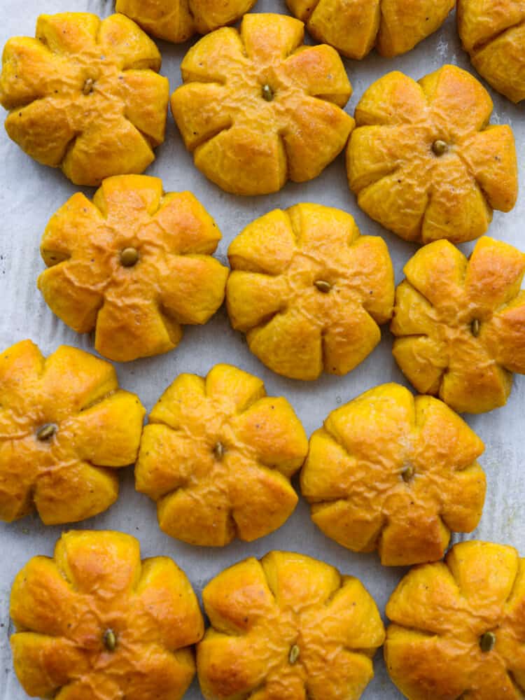 These pumpkin dinner rolls are the perfect, festive side dish to add to any fall meal! They not only taste like pumpkin but they are shaped just like one as well! Impress all of your guests by making these rolls and taking your holiday celebrations to the next level. The top view of pumpkin rolls on a baking sheet.