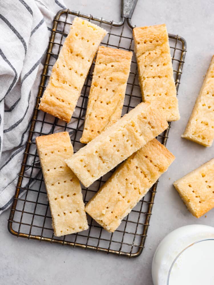 Traditional Scottish shortbread is buttery, crispy, and lightly sweetened to perfection. Simply made with butter, flour, sugar, and salt, this classic treat can easily be made for the holidays or any time of year. Top view of pieces of shortbread on a gray counter and a cooling rack. A glass of milk and kitchen towel are next to the cookies.