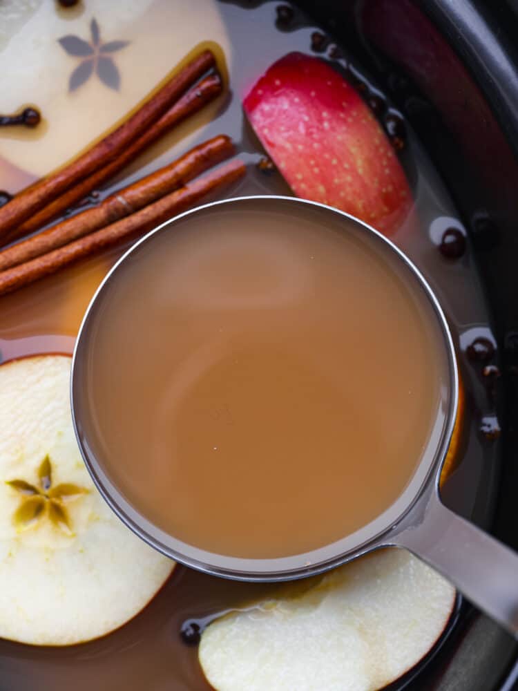 This easy crockpot apple cider is the must-have drink for this fall and winter! It has all the right spices and flavors and will warm you right up on those cold winter days! It's perfect for any holiday party or gathering! A measuring cup filled with apple cider.