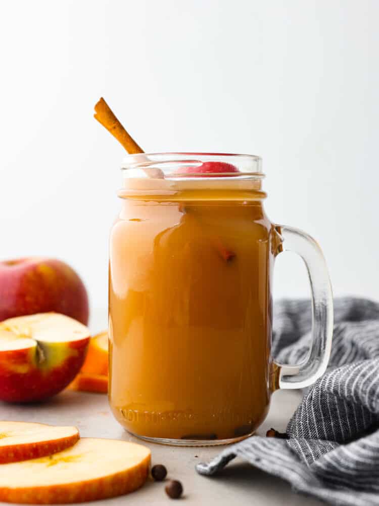 This easy crockpot apple cider is the must-have drink for this fall and winter! It has all the right spices and flavors and will warm you right up on those cold winter days! It's perfect for any holiday party or gathering! a mason jar with a handle filled with apple cider and topped with a cinnamon stick.