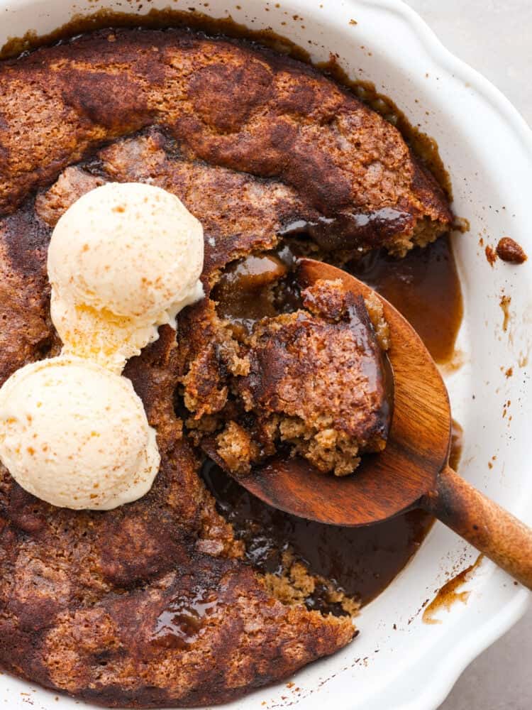 Snickerdoodle cobbler is loaded with cinnamon and creates its own caramel sauce while it bakes! It's soft, sweet and so delicious. It makes the perfect fall dessert that all of your guests will be dying to try! A close up of snickerdoodle cobbler being scooped out with a wooden spoon. A scoop of vanilla ice cream is on top.