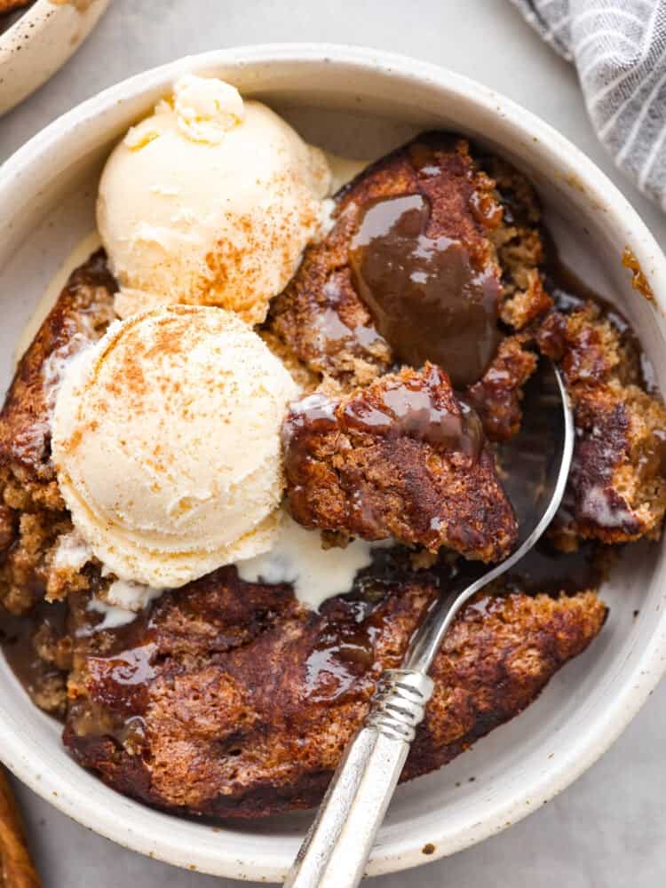 Snickerdoodle cobbler is loaded with cinnamon and creates its own caramel sauce while it bakes! It's soft, sweet and so delicious. It makes the perfect fall dessert that all of your guests will be dying to try! A closeup of snickerdoodle cobbler with ice cream and a silver spoon scooping some out of a white bowl.