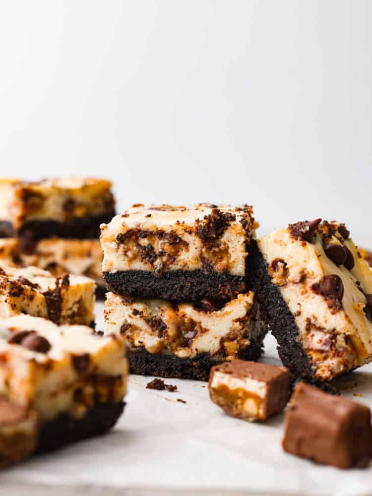 With a rich oreo crust and Snickers-filled cheesecake topping, these Snickers cheesecake bars are one of the best desserts out there! They're creamy, chocolatey, and sure to be loved by everyone! This is your sign to make a double batch. Snickers cheesecake bar slices stacked on top of each other.