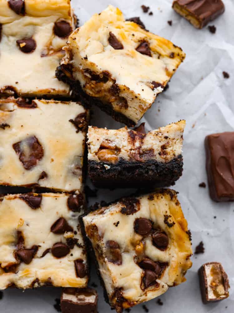 With a rich oreo crust and Snickers-filled cheesecake topping, these Snickers cheesecake bars are one of the best desserts out there! They're creamy, chocolatey, and sure to be loved by everyone! This is your sign to make a double batch. Top-down view of sliced Snickers dessert bars.