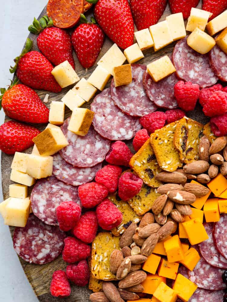 Gobble gobble your way to Thanksgiving dinner with the cutest turkey charcuterie board there ever was! Guests of all ages will love this fun way to enjoy a snack or appetizer full of meat, cheese, crackers, and lots of fruit! Close overhead view of charcuterie ingredients. Strawberries, salami, cheeses, raspberries, crackers, and almonds are arranged on the board.