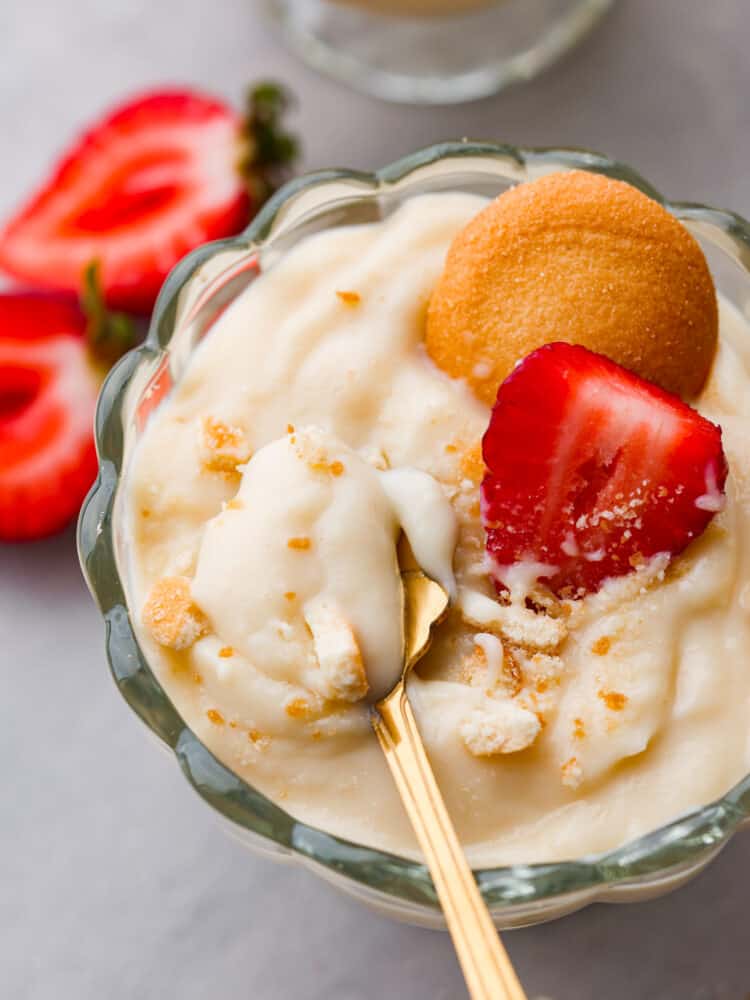If you're looking for a tried and true vanilla pudding recipe, this is it! This homemade vanilla pudding is perfectly sweet, silky smooth, and really easy to make! Closeup of vanilla pudding in a glass cup topped with a Nilla Wafer and sliced strawberry.