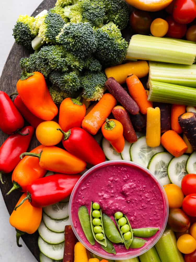 Every get-together needs a nutritious veggie charcuterie board full of colorful vegetables beautifully displayed all together. Perfect as an appetizer or side dish, this healthy board of fresh veggies is a hit served with a side of hummus and ranch dressing. Top view of the beet hummus with sugar snap peas garnished on top. Veggies are surrounding the hummus.