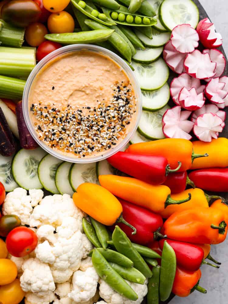 Every get-together needs a nutritious veggie charcuterie board full of colorful vegetables beautifully displayed all together. Perfect as an appetizer or side dish, this healthy board of fresh veggies is a hit served with a side of hummus and ranch dressing. Top view of hummus surrounded by lots of veggies. Bagel seasoning is sprinkled on top of the hummus.