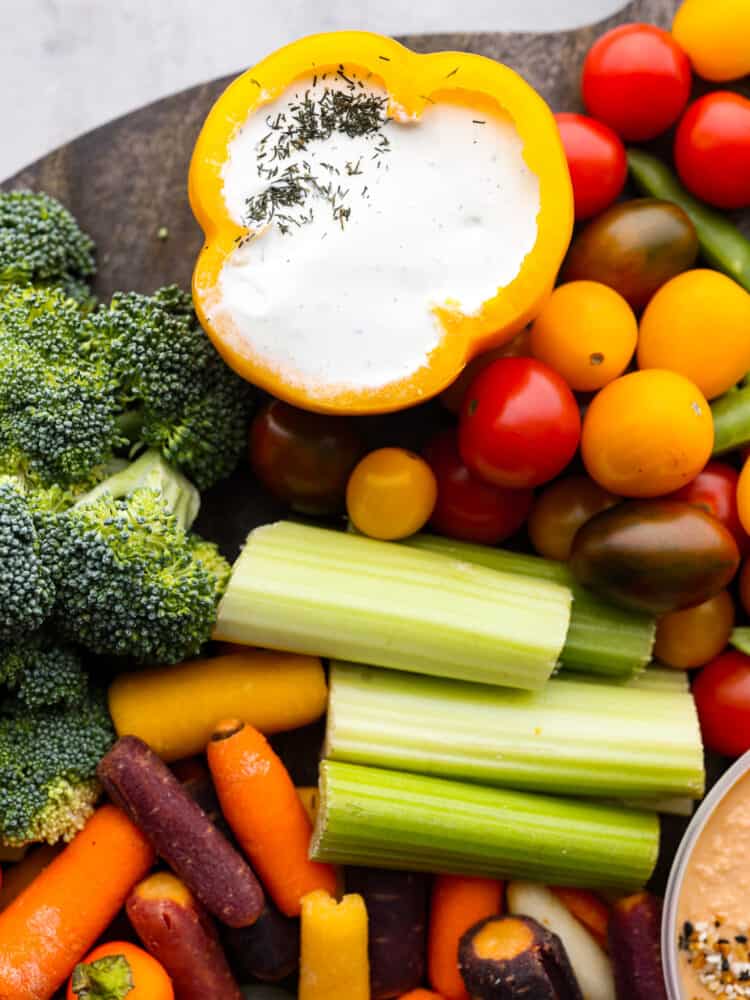 Every get-together needs a nutritious veggie charcuterie board full of colorful vegetables beautifully displayed all together. Perfect as an appetizer or side dish, this healthy board of fresh veggies is a hit served with a side of hummus and ranch dressing. Top view of ranch dip inside a bell pepper. Veggies are surrounding the the dip on the charcuterie board.