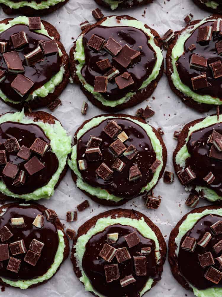 These Andes mint cookies are chewy and soft, topped with a lovely mint frosting and silky chocolate ganache. Andes mint candies sit on top and melt into the cookie as you chew, making it the perfect bite every time! Andes mint cookies on parchment paper.