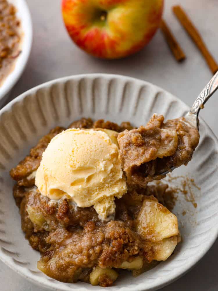 An Apple Brown Betty is a warm and comforting apple dessert that is full of fall flavors. The apples are coated in lemon juice with a brown sugar spiced crumble throughout that satisfies with every bite. If you don't like oats, this recipe is for you! A slice of brown apple betty on a white ribbed plate with a fork taking a bite out of it.