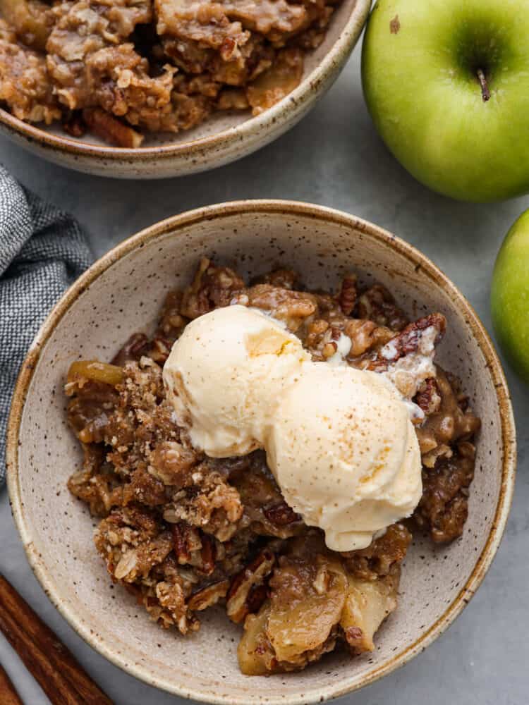 Apple pecan crisp is so easy to make and is the perfect fall dessert! The crisp apples, crunchy pecans hidden throughout, and a buttery cinnamon sugar crumb topping are the perfect combo! A bowl of apple pecan crisp with 2 scoops of vanilla ice cream on top,.