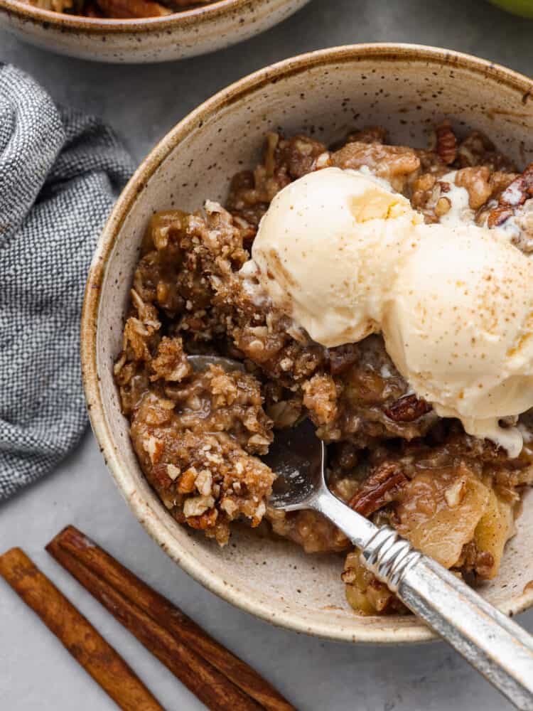 Apple pecan crisp is so easy to make and is the perfect fall dessert! The crisp apples, crunchy pecans hidden throughout, and a buttery cinnamon sugar crumb topping are the perfect combo! A bowl of apple pecan crisp with ice cream in a bowl with a silver spoon scooping some out.