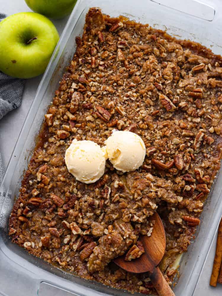 Apple pecan crisp is so easy to make and is the perfect fall dessert! The crisp apples, crunchy pecans hidden throughout, and a buttery cinnamon sugar crumb topping are the perfect combo! A top view of apple pecan crisp in a 9 x 13 pan with 2 scoops of vanilla ice cream on top.