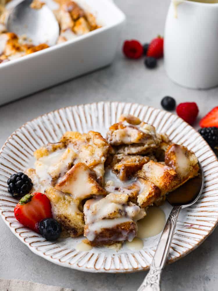 This Bread Pudding is a classic dessert that uses your leftover bread and a delicious vanilla sauce to make the best breakfast dessert you've ever had! It's frugal and cheap to make, but the flavor is out of this world divine. Bread pudding on a plate with fresh strawberries and blackberries and blueberries and a metal spoon.