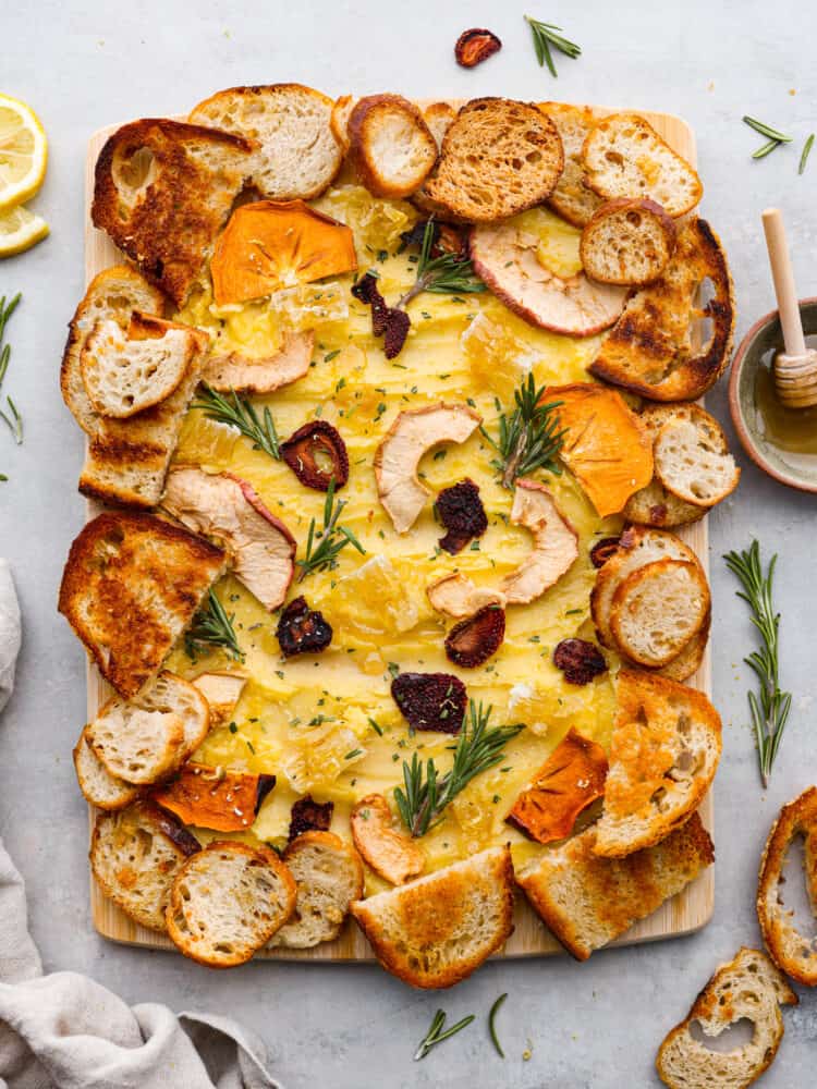 A butter board is the latest trend that you absolutely MUST TRY for your next gathering! This board is packed with the most delicious butter that is drizzled with honey and lemon zest and adds the perfect touch to your favorite bread! The top view of a butter board garnished with dried fruits, rosemary sprigs and crostini.