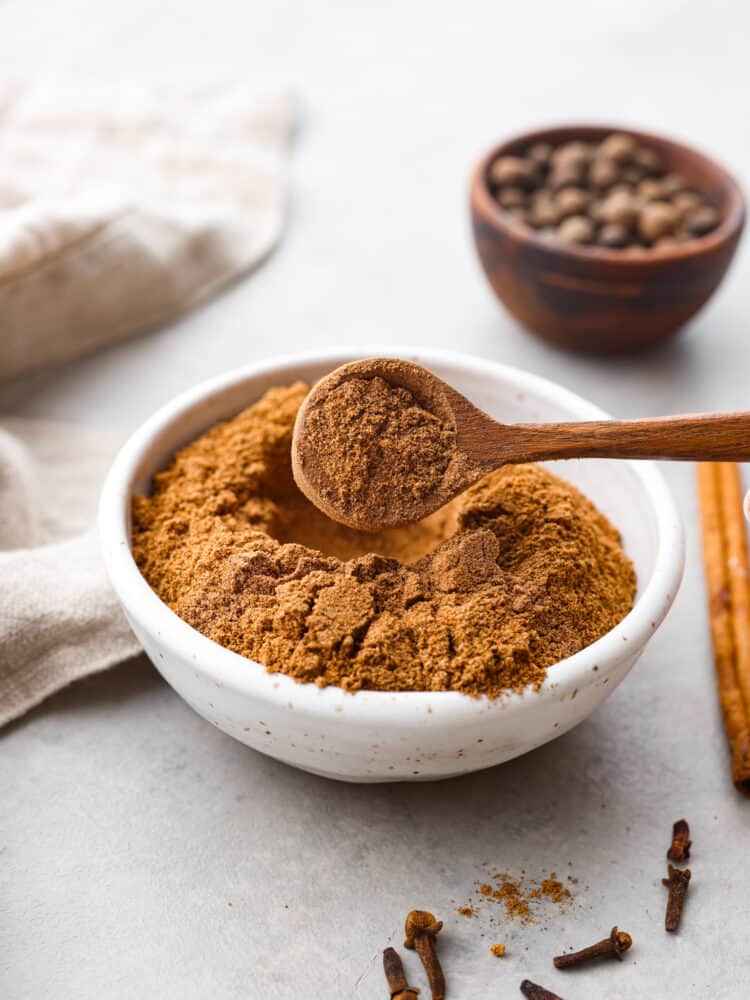 There are so many great reasons to make Chai Spice at home! It is a blend of warm fall spices that make it perfect for cakes, cookies, and even your coffee or tea! Chai Spice in a bowl with a wooden spoon that has taken a spoon full with spices in the foreground and background.