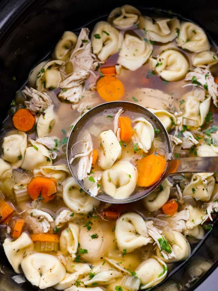 Slow cooker chicken tortellini soup is loaded with chopped vegetables, shredded cooked chicken, and cheesy tortellini all slow-cooked in a flavorfulย chicken broth. It's definitely a dinner the whole family will love! A closeup of chicken tortellini soup being scooped out of a crockpot with a ladle.