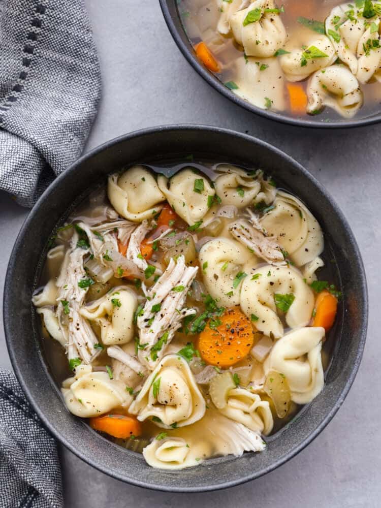 Slow cooker chicken tortellini soup is loaded with chopped vegetables, shredded cooked chicken, and cheesy tortellini all slow-cooked in a flavorfulย chicken broth. It's definitely a dinner the whole family will love! A gray bowl filled with chicken tortellini soup.