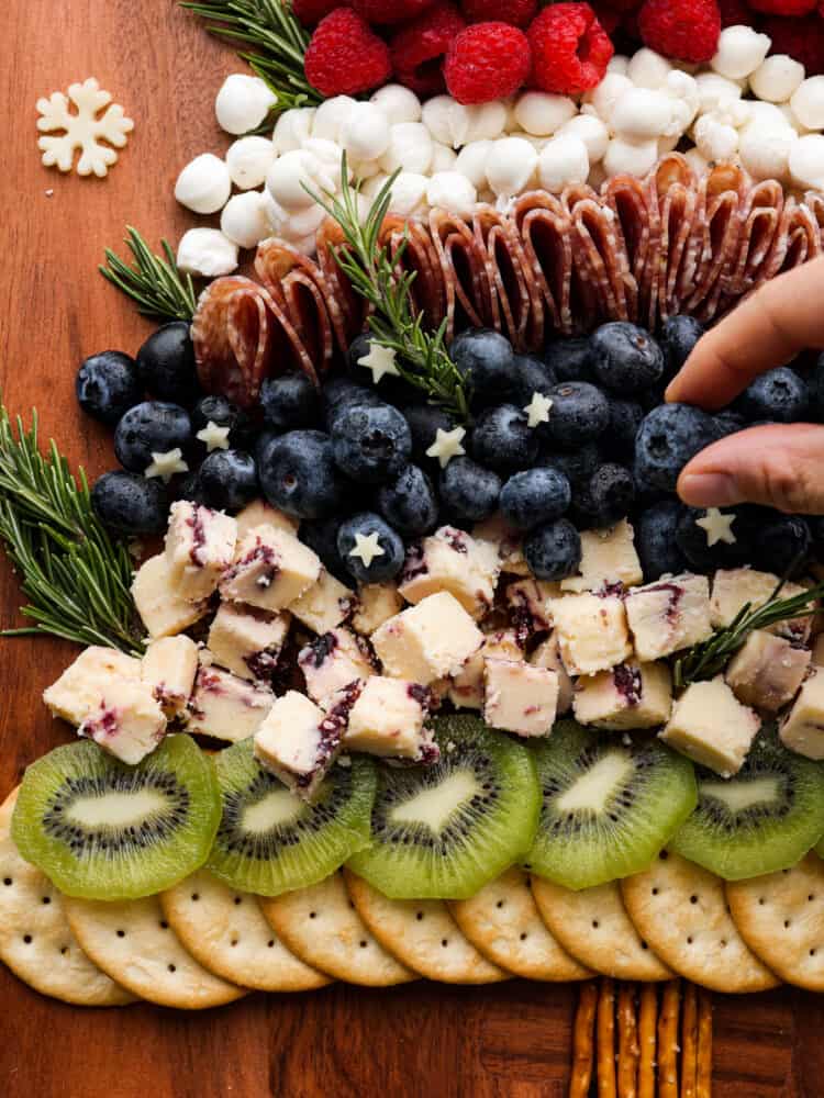 The cutest addition to any holiday party, this Christmas tree charcuterie board is both festive and delicious! It features a delicious mix of salami, prosciutto, cheese, fruits, and nuts, with rosemary sprigs as tree branches! It almost looks too good to eat. Closeup of cheese and berry layers on charcuterie board.