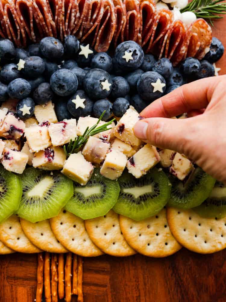 The cutest addition to any holiday party, this Christmas tree charcuterie board is both festive and delicious! It features a delicious mix of salami, prosciutto, cheese, fruits, and nuts, with rosemary sprigs as tree branches! It almost looks too good to eat. Adding cubes of Wensleydale cheese to the charcuterie board.