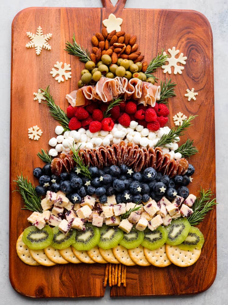 The cutest addition to any holiday party, this Christmas tree charcuterie board is both festive and delicious! It features a delicious mix of salami, prosciutto, cheese, fruits, and nuts, with rosemary sprigs as tree branches! It almost looks too good to eat. Top-down view of a whole Christmas tree charcuterie board.