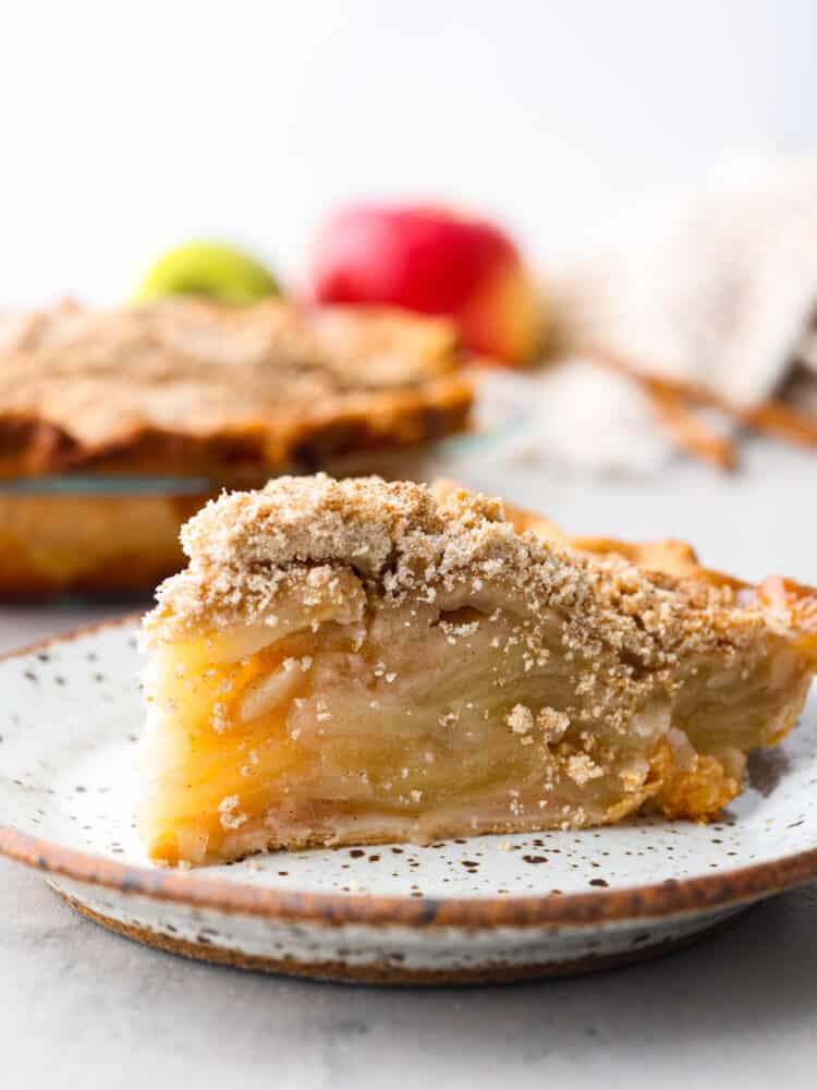 Dutch Apple Pie is the best version of apple pie! Instead of a top crust, you enjoy a sweet crumble topping over a mound of delicious apples. Everyone will agree that this is the best apple pie they've ever had. Closeup of a slice of apple pie on a stoneware plate.