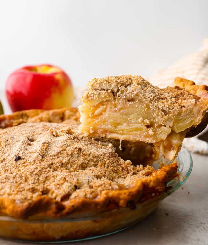 Dutch Apple Pie is the best version of apple pie! Instead of a top crust, you enjoy a sweet crumble topping over a mound of delicious apples. Everyone will agree that this is the best apple pie they've ever had. A slice being cut out of the pie and lifted out with a cake spatula.