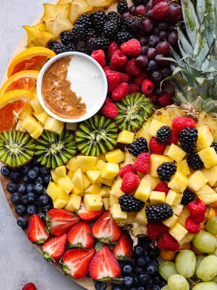 You will love the vibrant colors of all your favorite fruits beautifully displayed together on a fruit charcuterie board. Serve this as a perfect side dish or dessert at your next party alongside a creamy fruit dip! Close overhead view of the kiwi, pineapple, berries, starfruit, orange slices, and fruit dip on the charcuterie board.