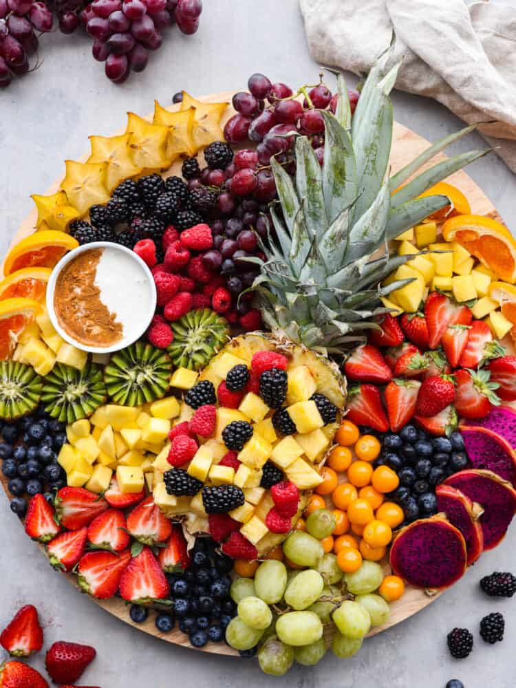 You will love the vibrant colors of all your favorite fruits beautifully displayed together on a fruit charcuterie board. Serve this as a perfect side dish or dessert at your next party alongside a creamy fruit dip! Overhead view of the fruit charcuterie board. A tan kitchen towel and extra fruit is scattered around the board.