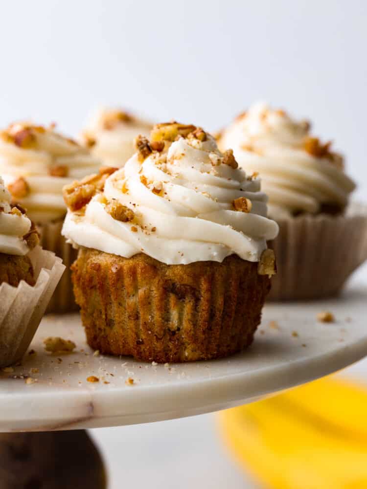 A bite-sized take on a classic Southern dessert, these hummingbird cupcakes are sure to win your heart! Filled with pecans, chopped fruit, and topped with smooth cream cheese frosting, you won't be able to stop at one! Frosted hummingbird cupcakes on a stone serving platter.