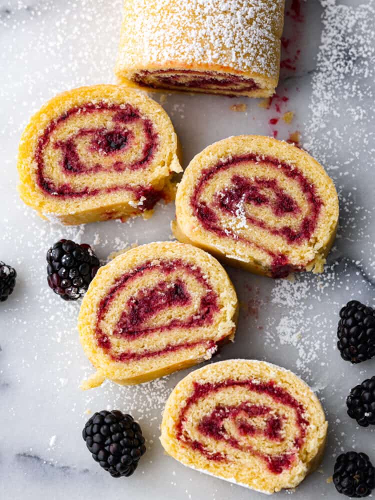 Jelly roll cake is a classic dessert that you need to make at least once! The chiffon cake is rolled with a delicious sweet jelly inside, and all of the flavors scream holiday cheer. You are going to love this easy-to-make dessert that looks stunning on the dinner table! Jelly roll cake cut up an laid out on the counter with powdered sugar sprinkled on top.