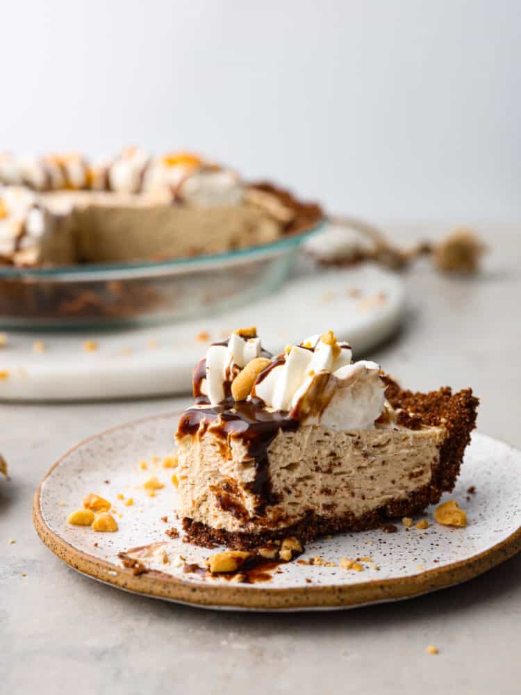 No-bake cream cheese peanut butter pie is an easy and amazing no-bake pie! The filling is so creamy and delicious inside a sweet, buttery, chocolate graham cracker crust. This is perfect for your next gathering! A slice of pie served on a stoneware plate, topped with chocolate drizzle.